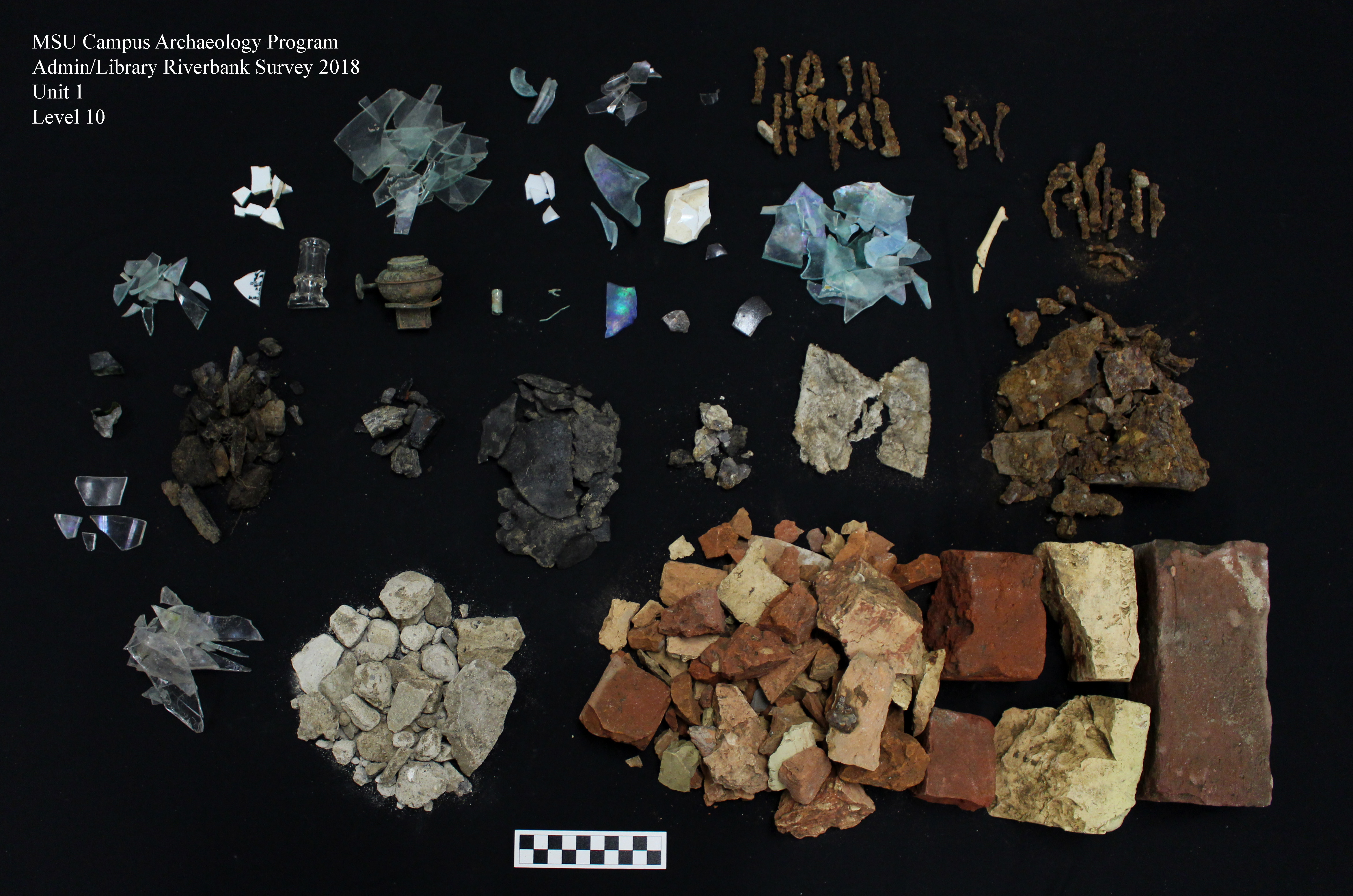Over twenty piles of different artifact types, including brick fragments, glass bottle shards, and nails